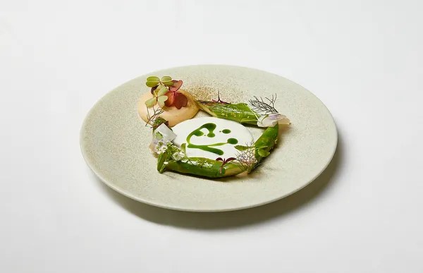 A Palate dish presented with green sauce and herb garnishes on a light-colored plate.