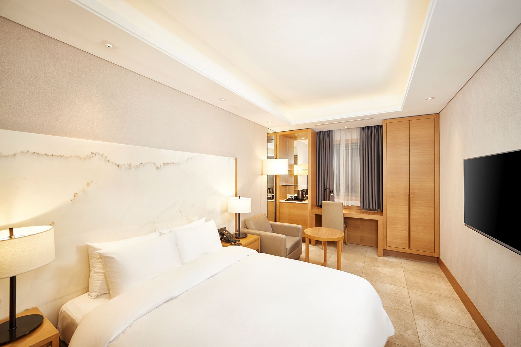 An Arban Hotel guest room with a double bed, bedside lighting, an armchair, table, desk and wardrobe.