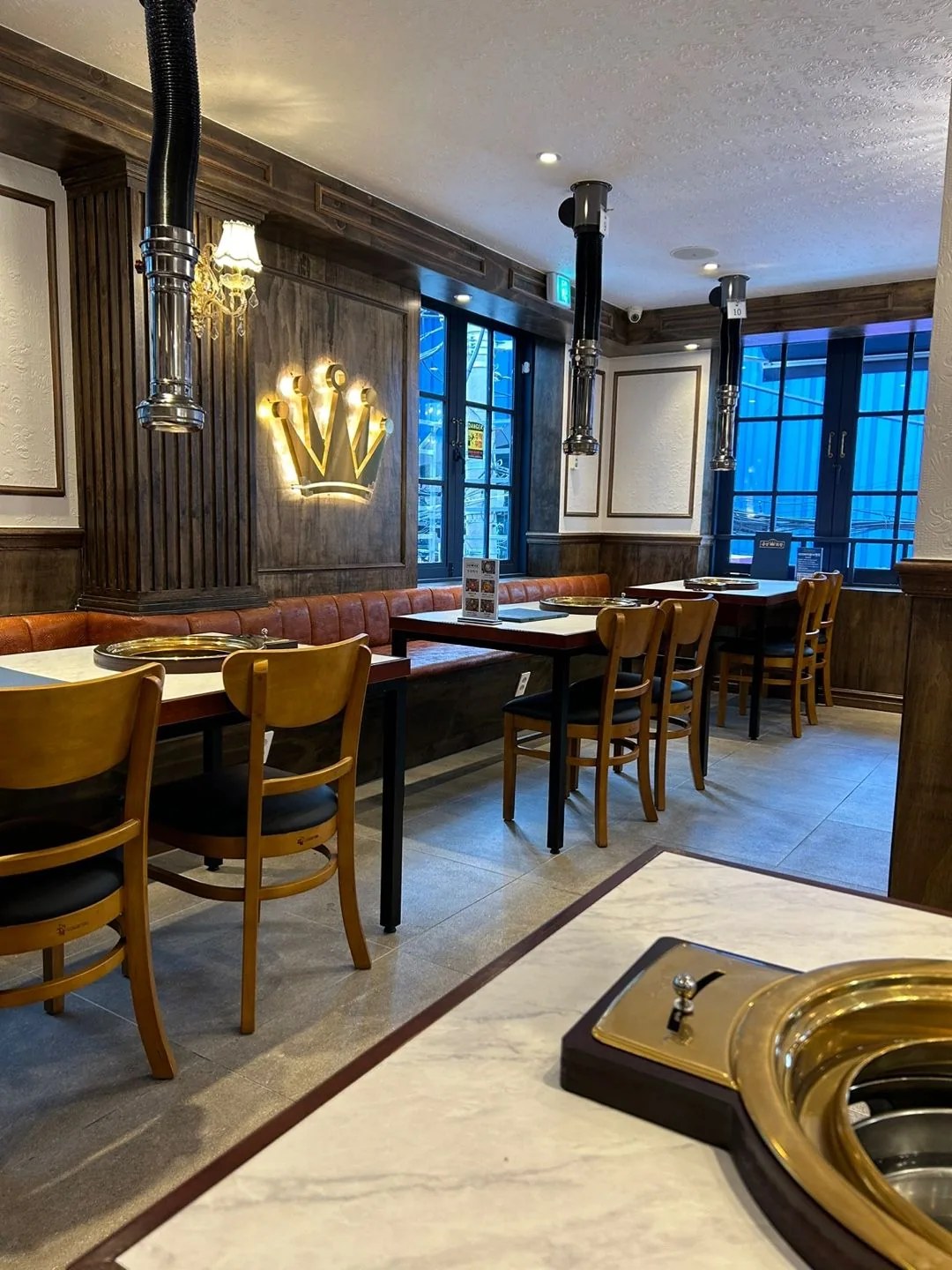 The dining room at Geumseong Hoegwan Busan Seomyeon, with a lit crown emblem, wood paneling and round brass grills.