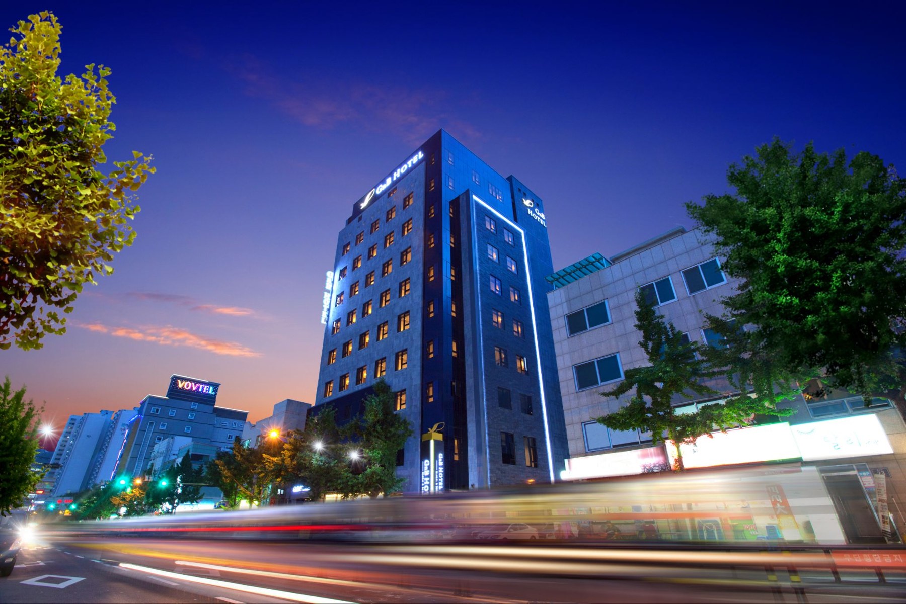 The exterior of GNB Hotel Busan at dusk, with its illuminated ‘GnB HOTEL’ signs.
