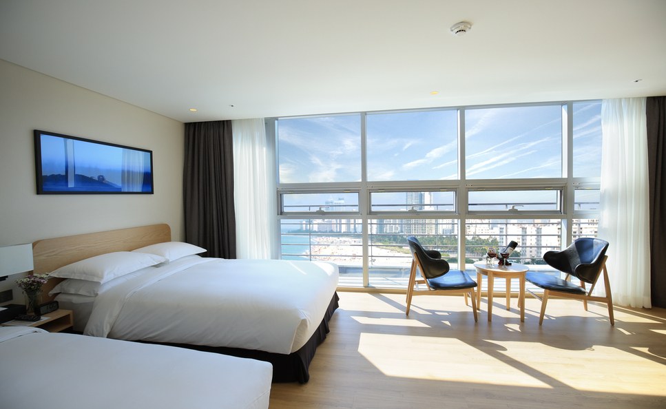A guest room at Best Western Haeundae Hotel with broad windows, a bed, chairs and a small table.
