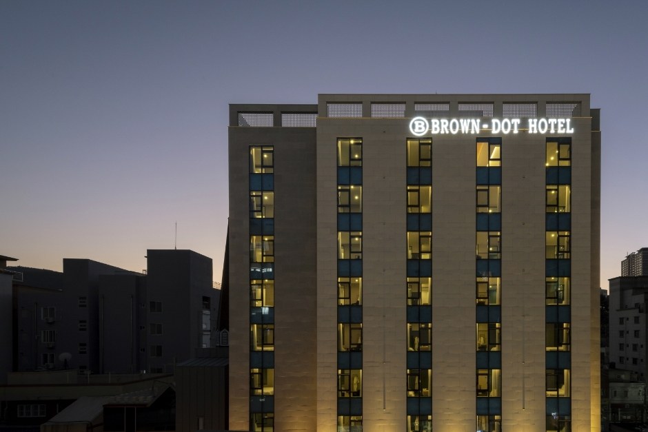 The Brown Dot Hotel exterior at dusk, with illuminated windows and its rooftop sign.